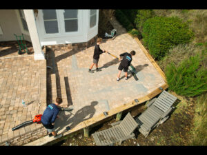 Workers applying paver sealing services on a residential patio in Ponte Vedra Beach, showcasing outdoor maintenance and cleaning efforts.