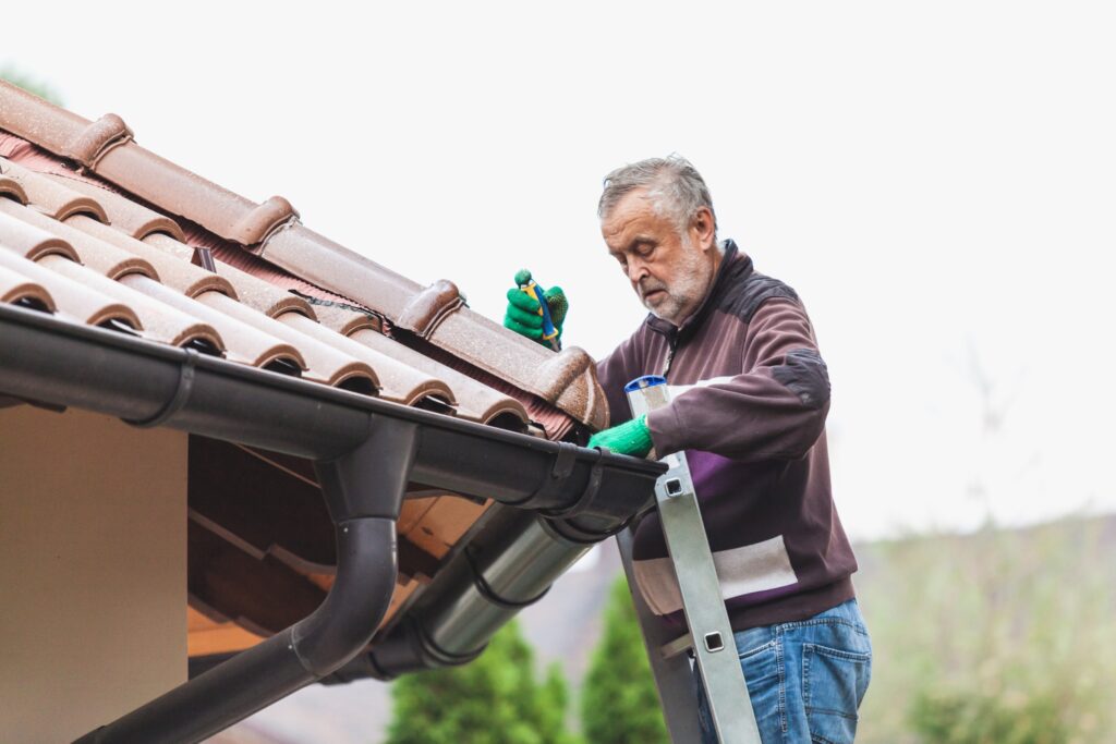 Man cleaning gutters on a roof using a ladder, highlighting the importance of gutter maintenance for home protection in Jacksonville.