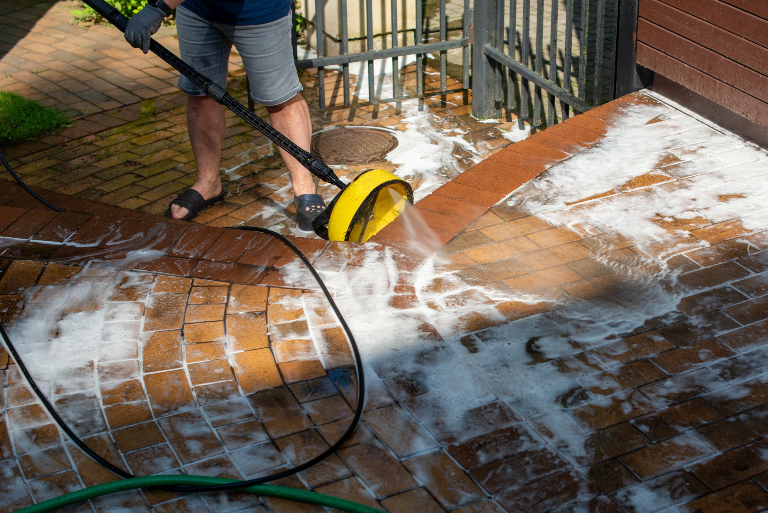 Person using a pressure washer on a brick patio, applying cleaning solution, showcasing effective patio cleaning practices in Florida.